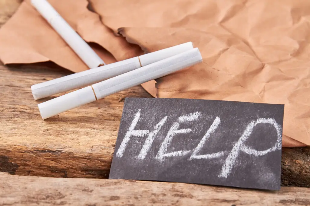 Help to overcome cigarette addiction. Text help, white tobacco cigarettes, burnt paper sheet, old wooden background.